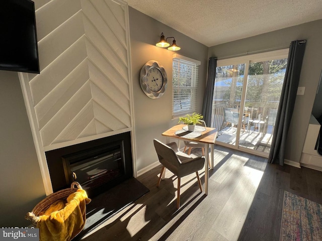 dining room with a textured ceiling, a fireplace, baseboards, and wood finished floors