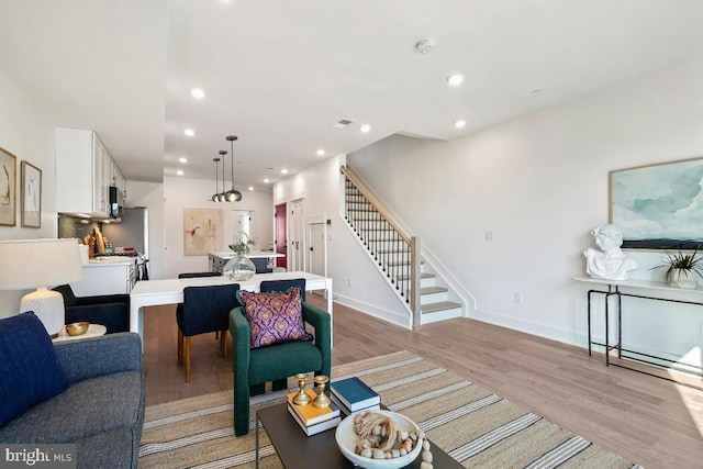 living area featuring light wood-style flooring, recessed lighting, stairway, and baseboards