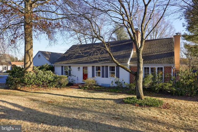 cape cod house featuring brick siding, a chimney, and a front yard