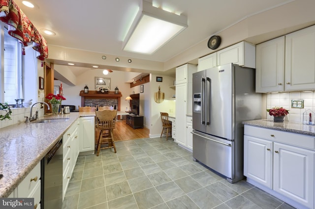 kitchen with light stone counters, appliances with stainless steel finishes, a sink, and white cabinetry