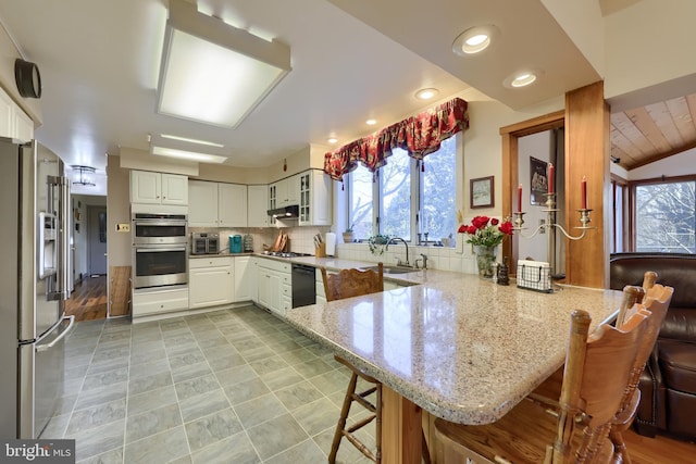 kitchen featuring appliances with stainless steel finishes, light stone counters, a peninsula, a kitchen bar, and white cabinetry