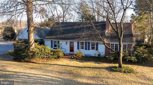 cape cod house featuring brick siding, a chimney, and a front yard