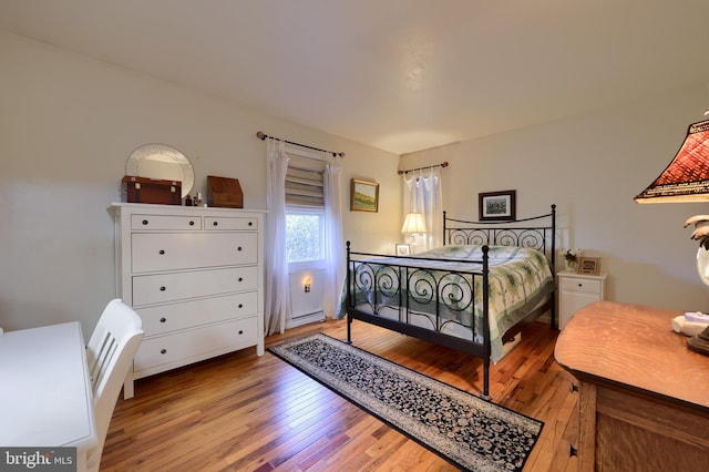 bedroom with light wood-type flooring and a baseboard heating unit