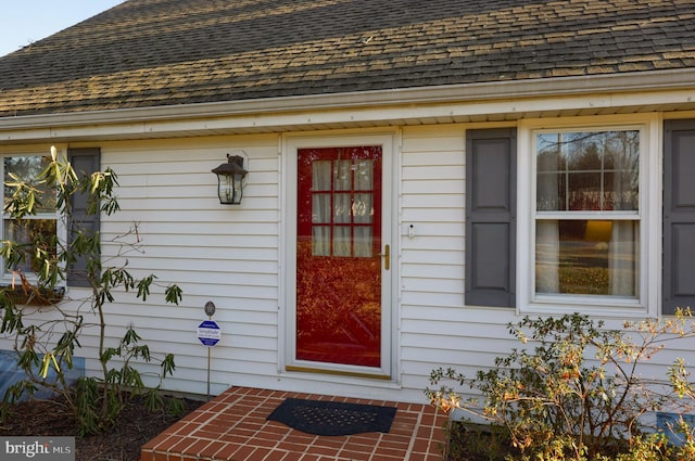 view of exterior entry featuring roof with shingles