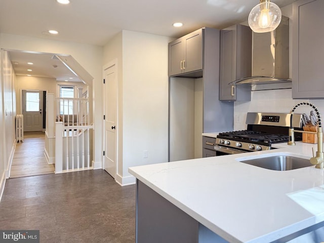 kitchen with gray cabinets, light countertops, stainless steel gas range oven, and wall chimney range hood