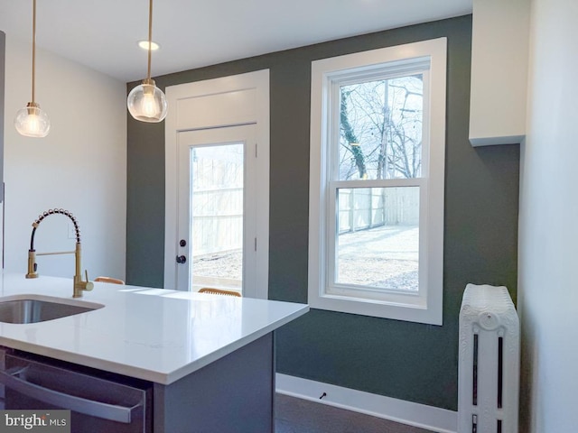 kitchen with baseboards, dishwasher, radiator heating unit, pendant lighting, and a sink