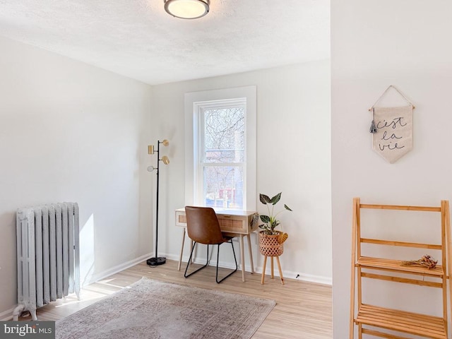 office space with a textured ceiling, baseboards, wood finished floors, and radiator