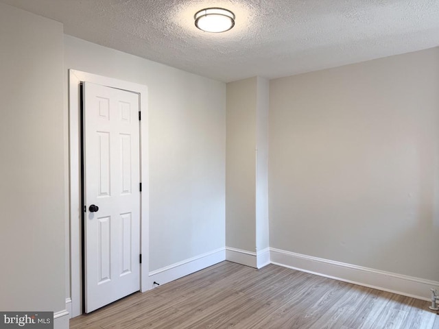 unfurnished room with a textured ceiling, baseboards, and wood finished floors