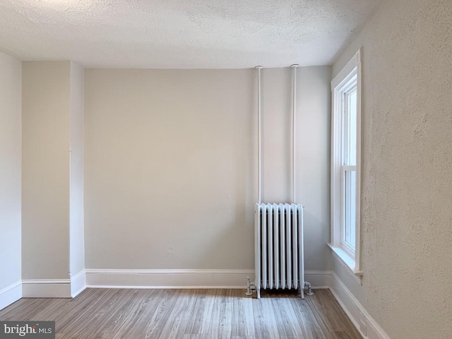 spare room with radiator, a healthy amount of sunlight, and wood finished floors