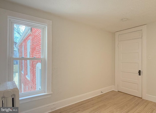 spare room featuring light wood finished floors, baseboards, and a textured ceiling