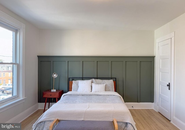 bedroom featuring baseboards, a decorative wall, and light wood finished floors