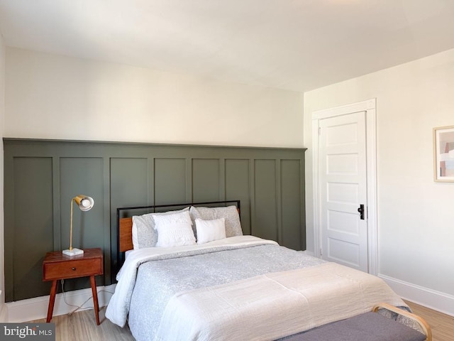 bedroom featuring light wood-type flooring, baseboards, and a decorative wall