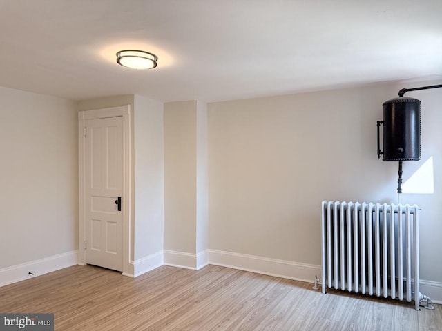 empty room featuring light wood finished floors, radiator heating unit, and baseboards