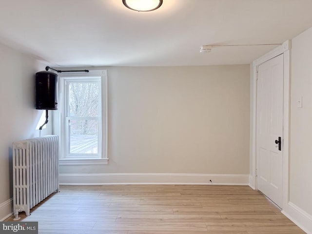 empty room featuring baseboards, light wood-style flooring, and radiator heating unit