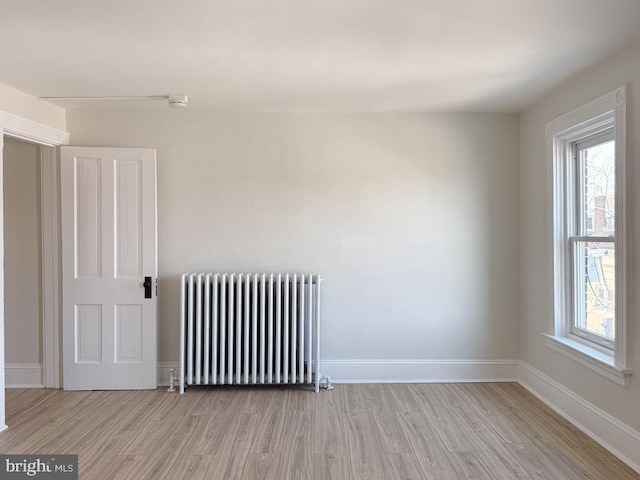 empty room with baseboards, wood finished floors, and radiator