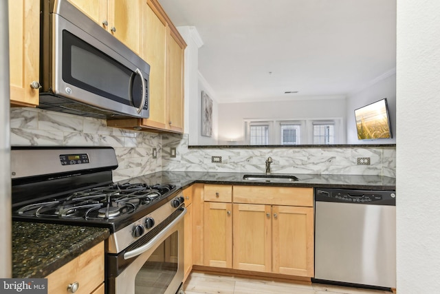 kitchen featuring crown molding, decorative backsplash, appliances with stainless steel finishes, a sink, and dark stone counters