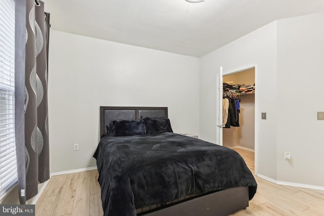 bedroom featuring light wood-type flooring, a walk in closet, and baseboards