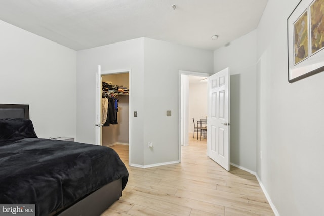 bedroom featuring light wood finished floors, a spacious closet, and baseboards