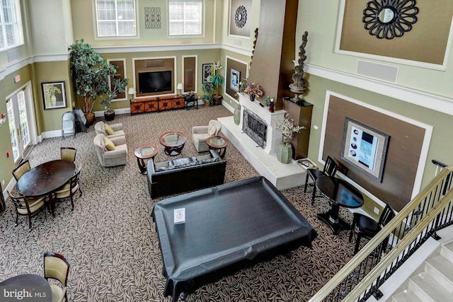 carpeted living area featuring a fireplace with raised hearth, a high ceiling, stairs, and a healthy amount of sunlight