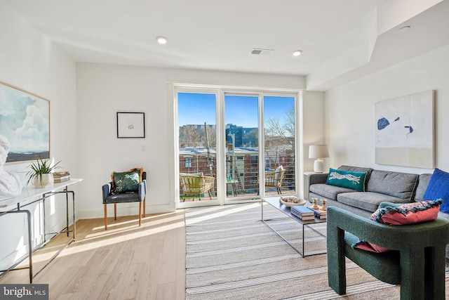 living room with recessed lighting, a city view, visible vents, baseboards, and light wood finished floors