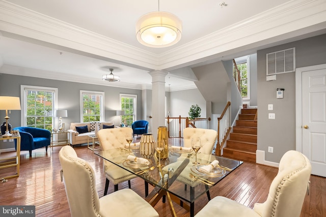 dining space featuring hardwood / wood-style floors, ornate columns, baseboards, ornamental molding, and stairs