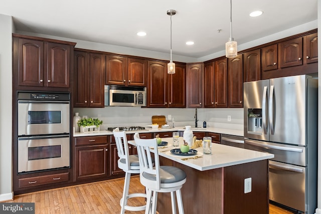 kitchen featuring appliances with stainless steel finishes, light wood finished floors, light countertops, dark brown cabinets, and recessed lighting