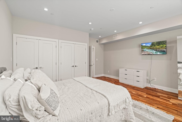 bedroom with recessed lighting, wood finished floors, visible vents, and two closets