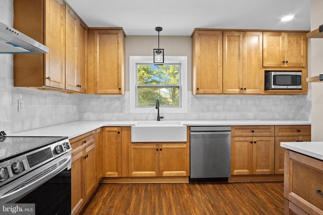 kitchen with appliances with stainless steel finishes, decorative light fixtures, light countertops, wall chimney range hood, and a sink