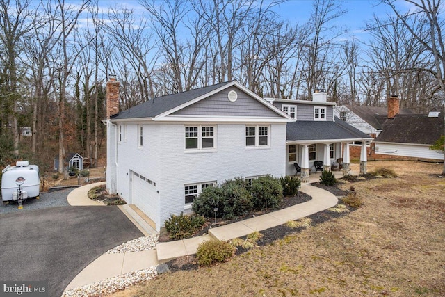 view of front of home with a garage, a chimney, aphalt driveway, covered porch, and brick siding