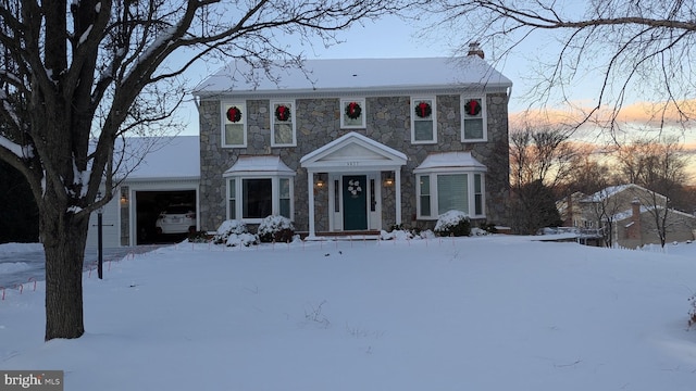 colonial house featuring an attached garage, stone siding, and a chimney