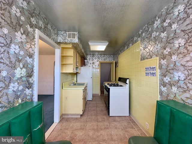 kitchen featuring open shelves, a sink, range with gas stovetop, wallpapered walls, and light countertops