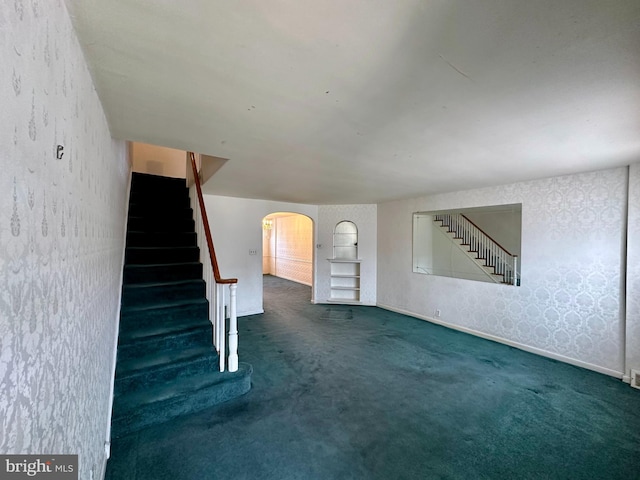 interior space featuring baseboards, arched walkways, carpet flooring, and wallpapered walls