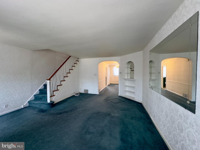 unfurnished living room with stairway, built in features, visible vents, wallpapered walls, and arched walkways