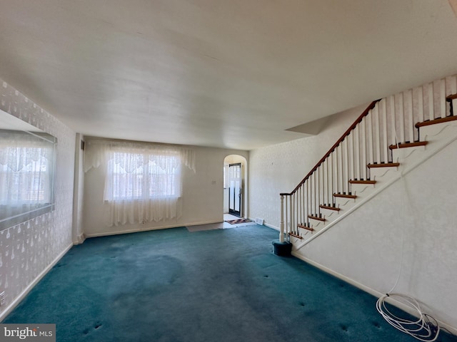 unfurnished living room featuring arched walkways, carpet flooring, and stairs