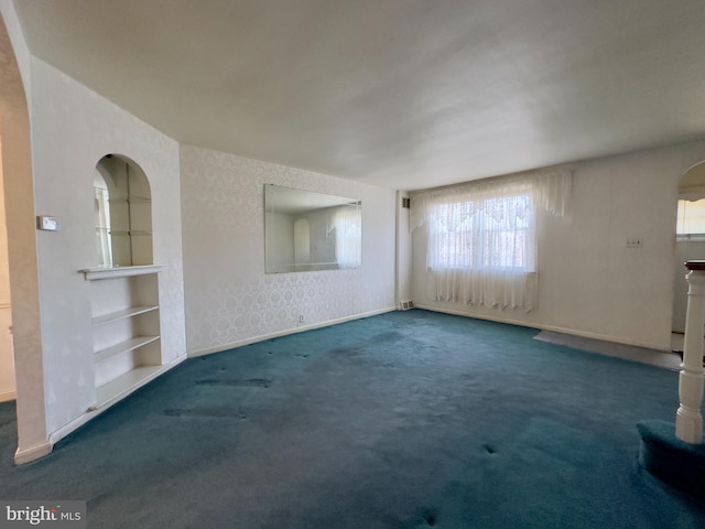 spare room with baseboards, arched walkways, carpet flooring, and wallpapered walls