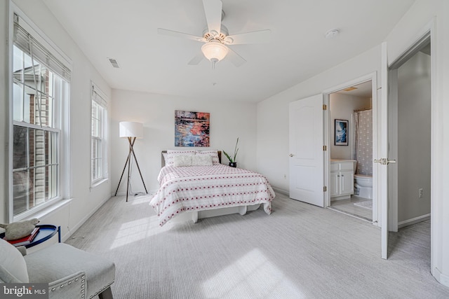 bedroom with light colored carpet, ceiling fan, visible vents, and ensuite bath