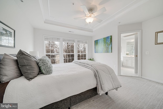 carpeted bedroom with ornamental molding, a tray ceiling, ensuite bath, and baseboards