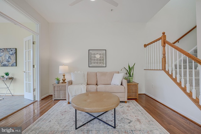 living area with a ceiling fan, stairway, baseboards, and wood finished floors