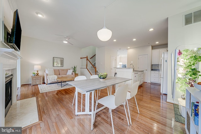 dining area featuring stairs, light wood-style flooring, a fireplace, and visible vents