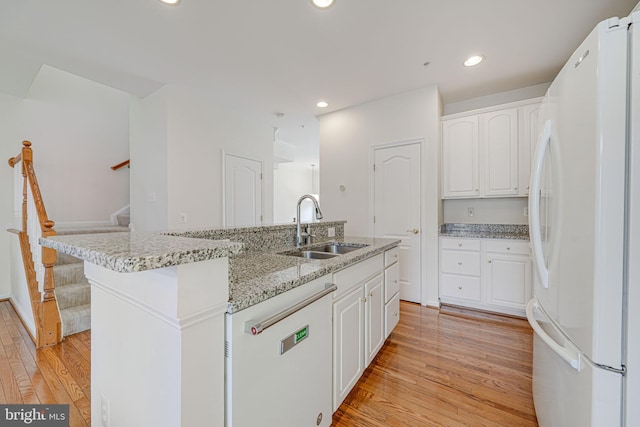 kitchen with an island with sink, dishwashing machine, freestanding refrigerator, white cabinetry, and a sink