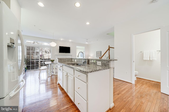 kitchen featuring stone counters, white cabinetry, a sink, an island with sink, and white appliances