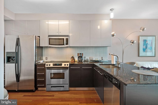 kitchen with stainless steel appliances, white cabinetry, a sink, dark stone countertops, and modern cabinets