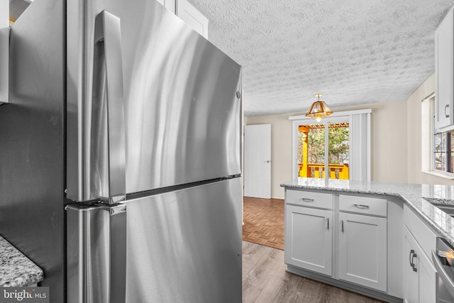 kitchen with a textured ceiling, stainless steel appliances, white cabinets, parquet floors, and light stone countertops