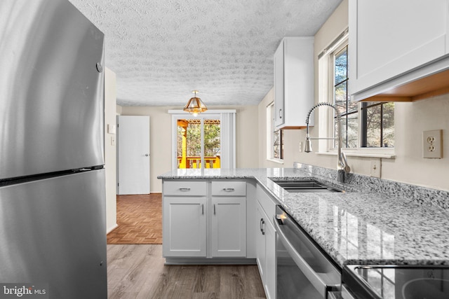 kitchen featuring light stone counters, hanging light fixtures, appliances with stainless steel finishes, white cabinetry, and a sink