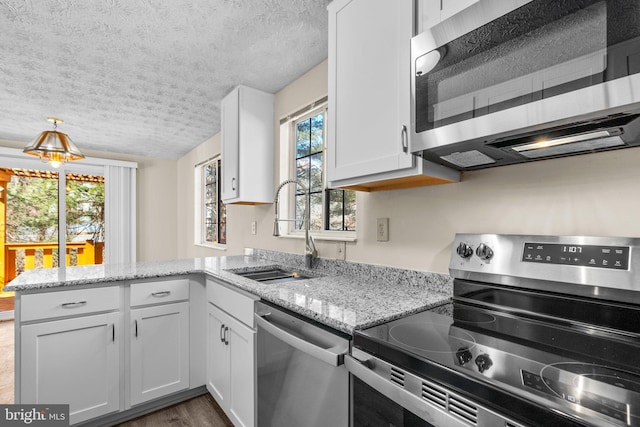 kitchen featuring stainless steel appliances, a peninsula, a sink, white cabinetry, and light stone countertops