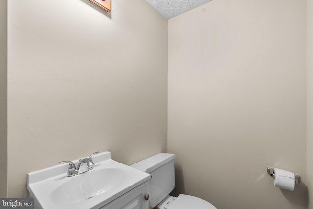 half bathroom featuring vanity, toilet, and a textured ceiling