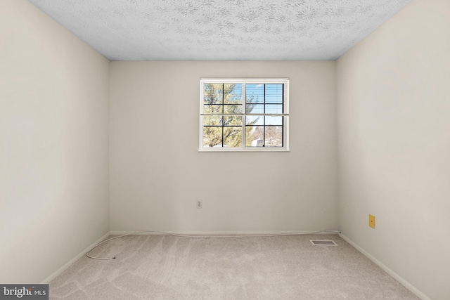 spare room with light carpet, a textured ceiling, visible vents, and baseboards