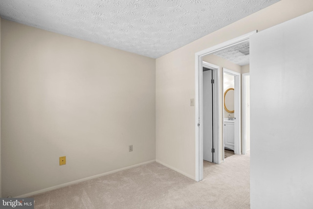 spare room featuring baseboards, a textured ceiling, and light colored carpet