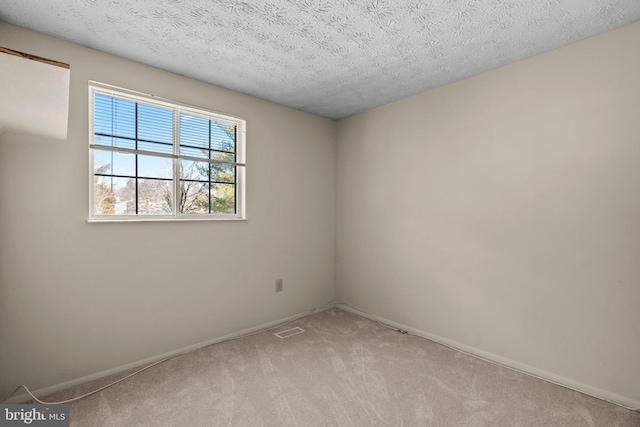 empty room with a textured ceiling, baseboards, visible vents, and light colored carpet