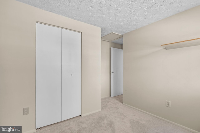 unfurnished bedroom with light carpet, attic access, baseboards, a textured ceiling, and a closet